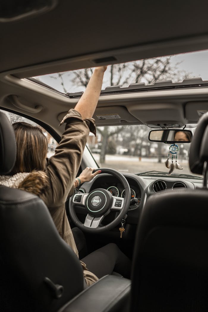 A young woman enjoying a drive with the sunroof open, showing car interior detail.